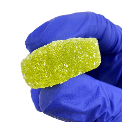 Gummies au THC verts goûts fraise tenu dans une main sur fond blanc